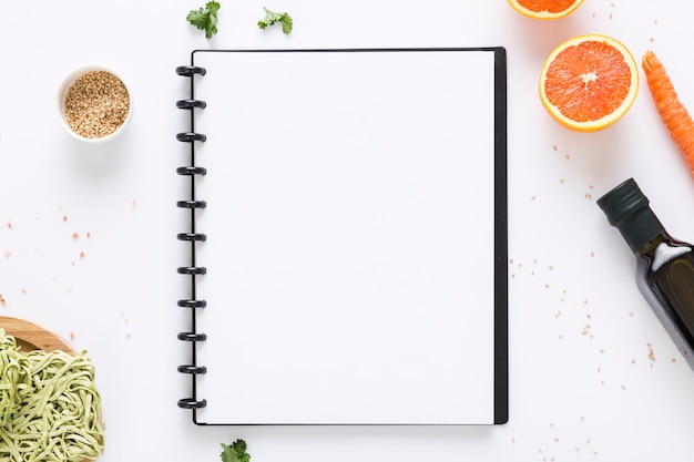 Vista superior del cuaderno de menú en blanco con aceite de oliva y zanahoria