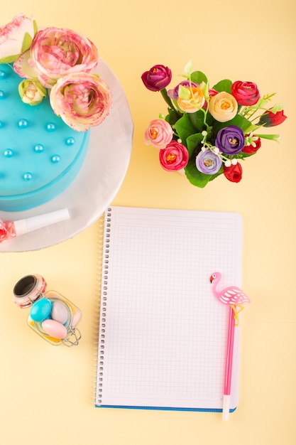 Una vista superior de cuaderno y pastel con flores en el color amarillo de la celebración de cumpleaños de la torta de escritorio