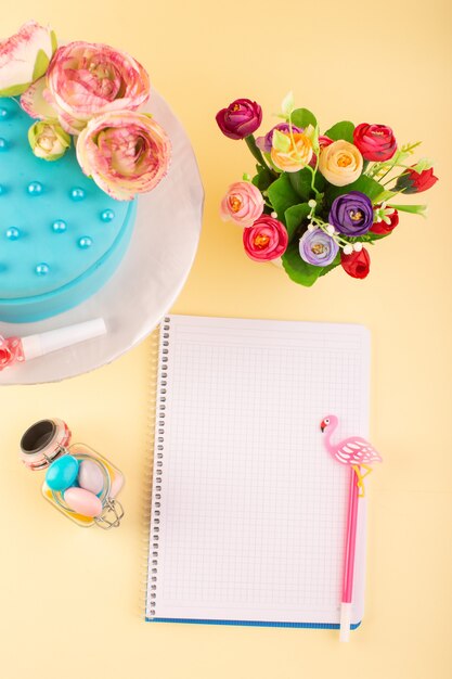 Una vista superior de cuaderno y pastel con flores en el color amarillo de la celebración de cumpleaños de la torta de escritorio