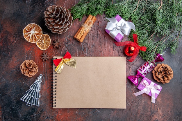 Vista superior de un cuaderno con pequeñas ramas de pino arco con conos y juguetes de árbol de Navidad rodajas de limón seco canela anises sobre fondo rojo oscuro