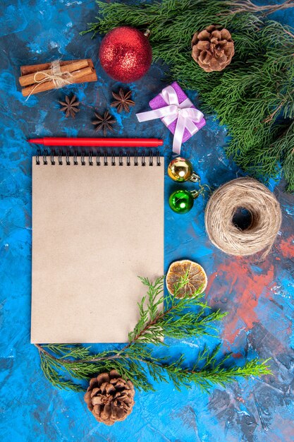 Vista superior de un cuaderno ramas de pino adornos de Navidad lápiz rojo sobre fondo azul.