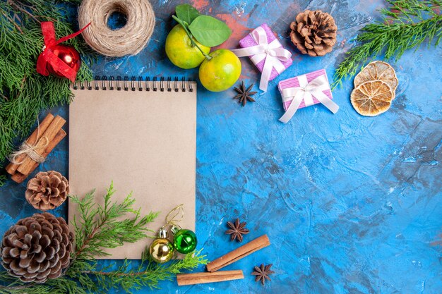 Vista superior de un cuaderno ramas de pino piña anís estrellado hilo de paja mandarinas canela sobre fondo azul espacio libre