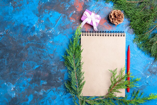 Vista superior de un cuaderno de ramas de pino piña lápiz rojo sobre fondo azul con espacio libre