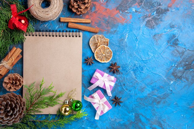 Vista superior de un cuaderno ramas de pino piñas anís estrellado bolas de árbol de navidad hilo de paja sobre fondo azul espacio libre