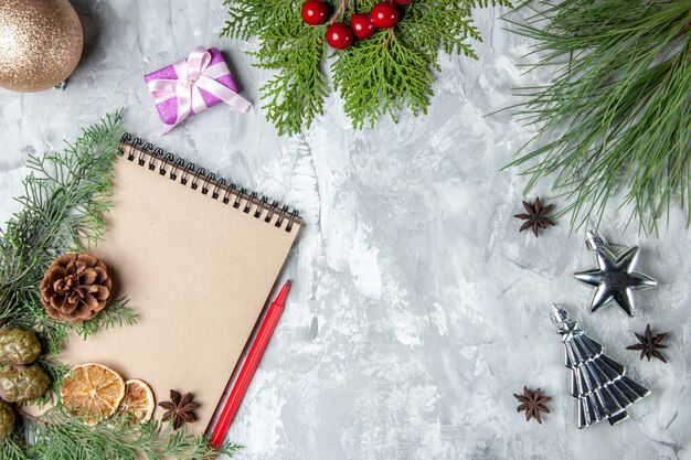 Vista superior del cuaderno de rodajas de limón secas anís ramas de los árboles de pino lápiz rojo juguetes del árbol de navidad sobre fondo gris espacio libre