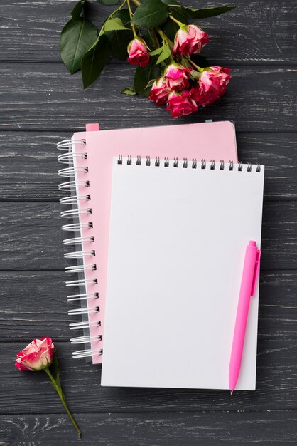 Vista superior de cuadernos en escritorio de madera con ramo de rosas