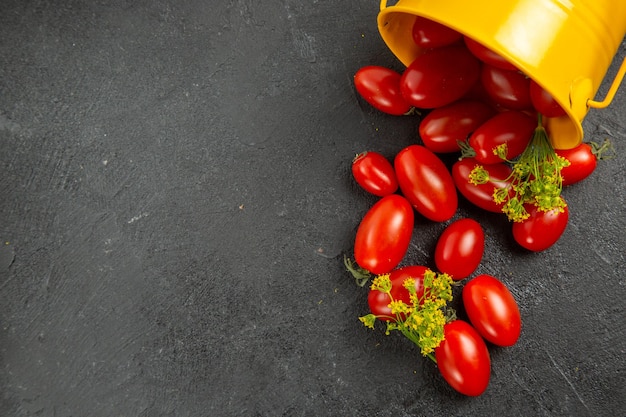 Vista superior del cubo amarillo volcado lleno de tomates cherry y flores de eneldo a la derecha del suelo oscuro con espacio de copia