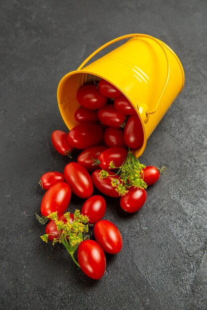 Vista superior del cubo amarillo volcado lleno de tomates cherry y flores de eneldo en el suelo oscuro