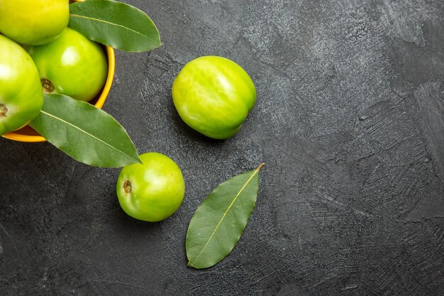 Vista superior del cubo de tomates verdes y hojas de laurel y tomates en una mesa oscura con espacio de copia