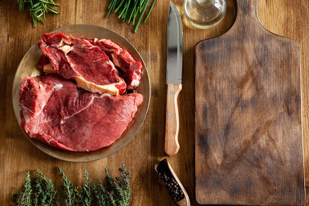 Vista superior del cuchillo de chef junto a grandes trozos de carne roja y verduras en la mesa de madera. Carne fresca.