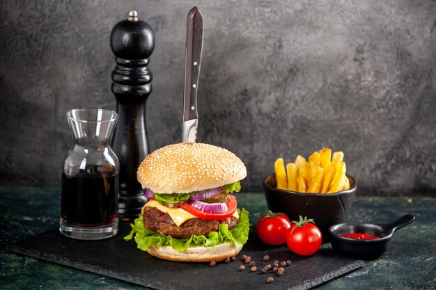 Vista superior del cuchillo en un delicioso sándwich de carne y pimiento verde en salsa de bandeja negra tomates ketchup con papas fritas en superficie oscura