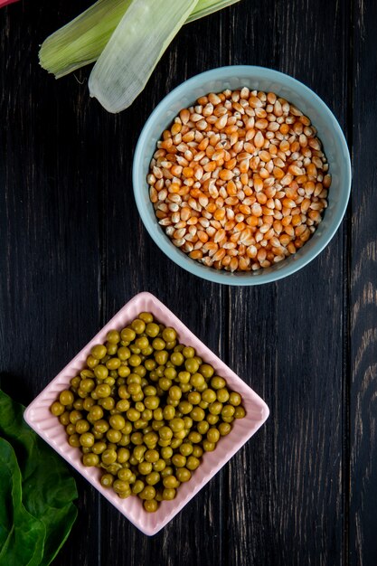 Vista superior de cuencos con semillas de maíz secas y guisantes verdes en superficie negra