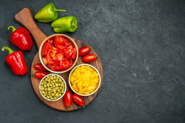 Vista superior de cuencos de verduras en el soporte del plato con verduras en el lateral y espacio libre para el texto sobre fondo gris oscuro