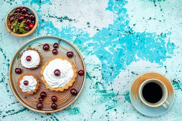 Vista superior de cupcake con crema y cerezas en la parte superior junto a una taza de café americano