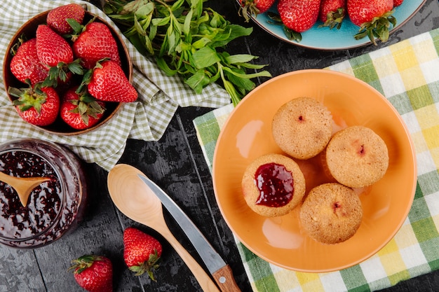 Vista superior cupcakes con mermelada de fresa, menta y fresas frescas sobre fondo negro