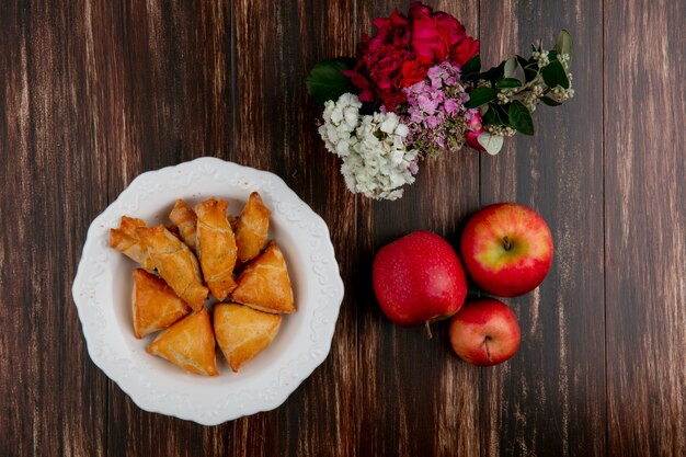 Vista superior curabier en un plato con manzanas rojas y flores sobre un fondo de madera