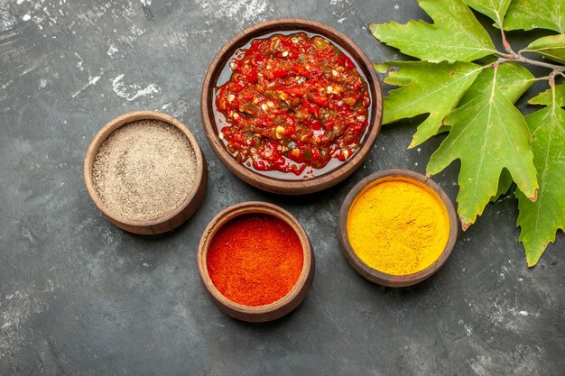 Vista superior de cúrcuma en polvo de ají picante adjika en tazones pequeños hojas sobre fondo gris