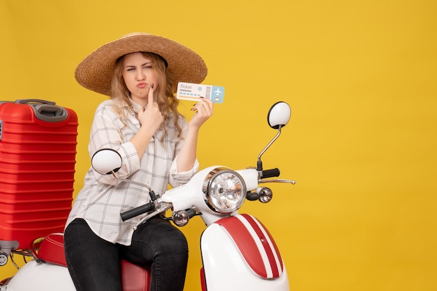 Vista superior de la curiosa joven con sombrero y sentada en una motocicleta y sosteniendo el boleto en amarillo