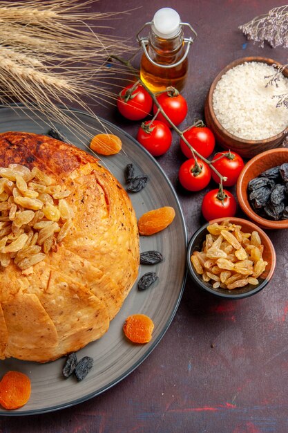 Vista superior de la deliciosa comida de arroz cocido de shakh plov con pasas y tomates en el escritorio oscuro con masa para cocinar la cena de arroz