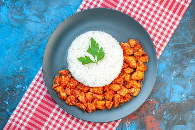 Vista superior de la deliciosa comida de arroz con pollo verde y tomate en una toalla despojada roja en la mesa azul