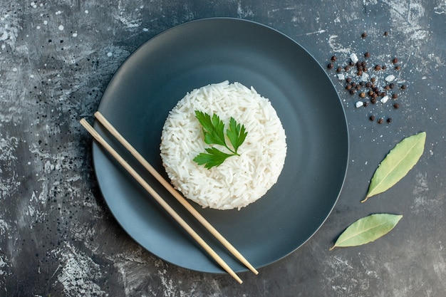 Vista superior de la deliciosa comida de arroz servida con palillos verdes y en un plato negro hojas de pimientos sobre fondo oscuro