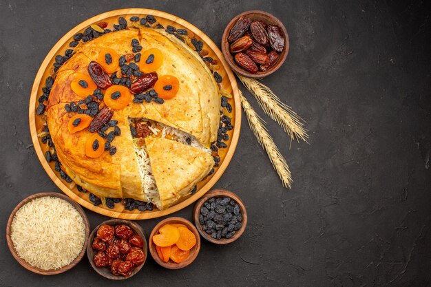 Vista superior de la deliciosa comida de arroz shakh plov cocinada dentro de masa redonda con pasas sobre una superficie gris oscuro