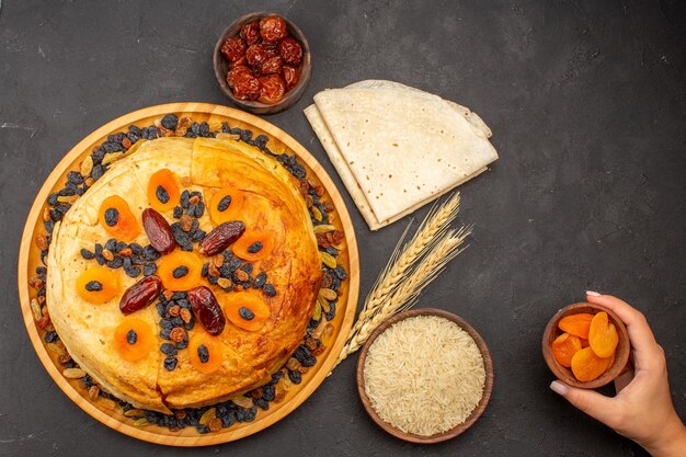 Vista superior de la deliciosa comida de arroz shakh plov cocinada dentro de masa redonda con pasas en la superficie gris