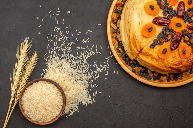 Vista superior de la deliciosa comida de arroz shakh plov cocinada dentro de masa redonda con pasas en la superficie gris