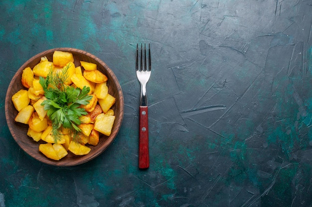 Vista superior de deliciosa comida de patatas en rodajas cocidas con verduras dentro de la placa marrón en el escritorio azul oscuro