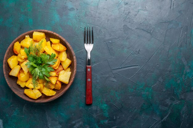 Vista superior de deliciosa comida de patatas en rodajas cocidas con verduras dentro de la placa marrón en el escritorio azul oscuro