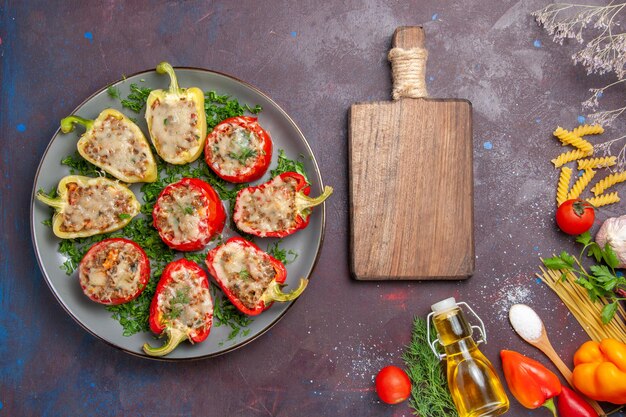 Vista superior de deliciosa comida de pimientos horneados con carne en el interior y verduras en el escritorio oscuro, cena, plato, comida, hornear