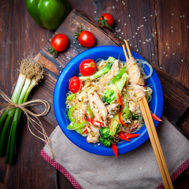 Foto gratuita vista superior deliciosa comida en placa azul con cebollas verdes, tomates y palillos sobre fondo de madera oscura.