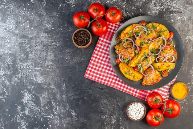 Vista superior de la deliciosa comida de pollo con papas y verduras en tomates de toalla pelado rojo doblado con especias de tallos en la mesa de color oscuro