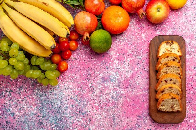 Vista superior de la deliciosa composición de frutas con tortas en rodajas en el escritorio rosa