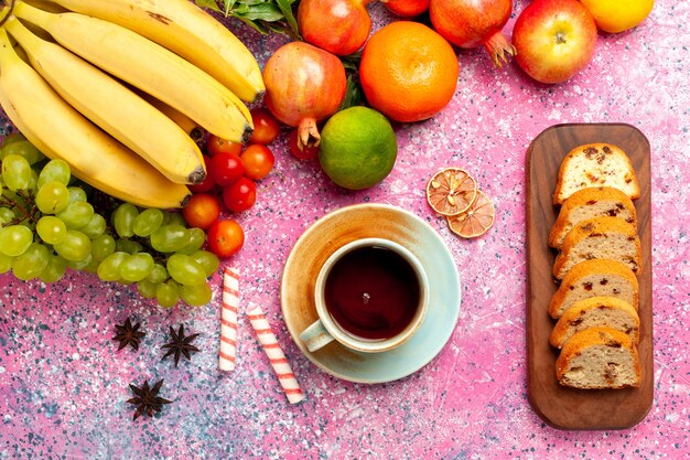 Vista superior de la deliciosa composición de frutas con tortas en rodajas en la superficie rosa