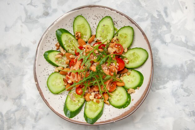 Vista superior de una deliciosa ensalada decorada con pepino picado y verduras en la superficie blanca manchada