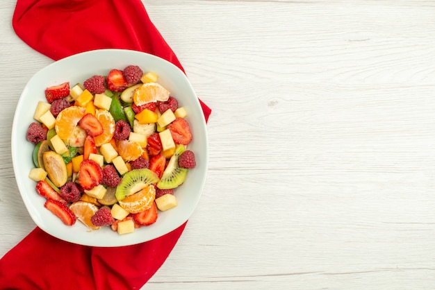 Vista superior deliciosa ensalada de frutas con tejido rojo sobre blanco exótico baya afrutada cítricos madura suave foto espacio libre