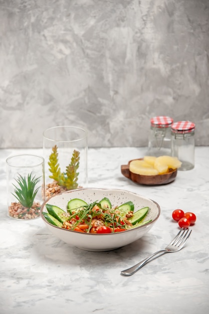 Vista superior de la deliciosa ensalada vegana casera decorada con pepinos picados en un tazón tenedor tomates piñas secas en la superficie blanca manchada