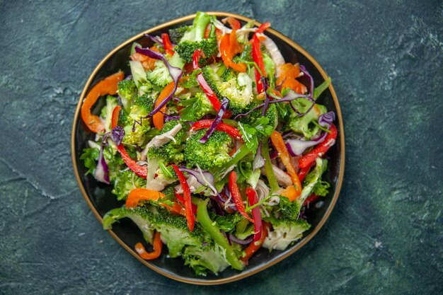 Vista superior de la deliciosa ensalada vegana en un plato con varias verduras frescas sobre fondo oscuro