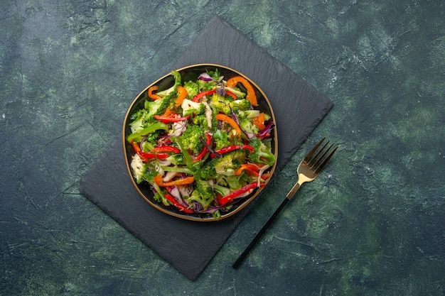 Vista superior de la deliciosa ensalada de verduras con varios ingredientes en la tabla de cortar negra