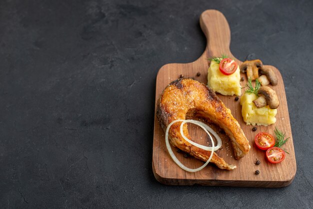 Vista superior de la deliciosa harina de pescado frito y champiñones tomates verdes en la tabla de cortar de madera en el lado izquierdo sobre la superficie negra