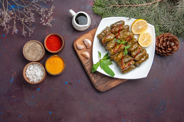 Vista superior de la deliciosa hoja dolma con rodajas de limón y condimentos en el fondo oscuro plato de comida de carne comida de cena de hoja