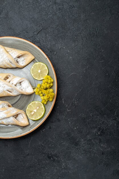 Vista superior deliciosa masa con azúcar en polvo y galletas en el escritorio gris oscuro pastelería hornear galletas de pastel dulce de azúcar