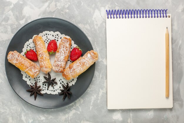 Vista superior de la deliciosa masa de bagels de azúcar en polvo con fresas y bloc de notas en la superficie blanca