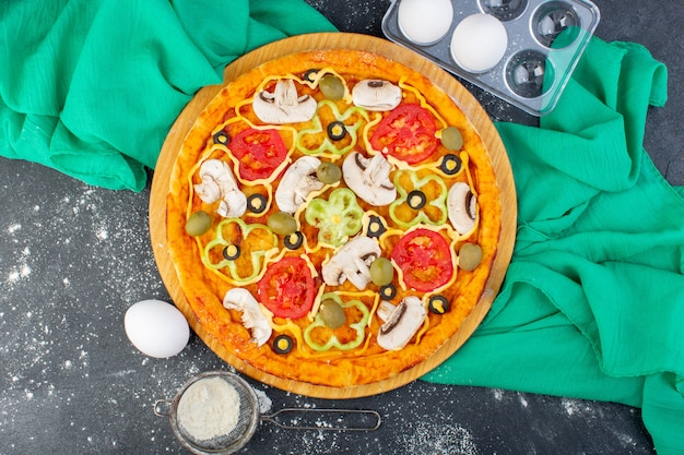 Vista superior deliciosa pizza de champiñones con tomates, aceitunas, champiñones, todos en rodajas con harina en el escritorio oscuro, masa de pizza de tejido verde, comida italiana