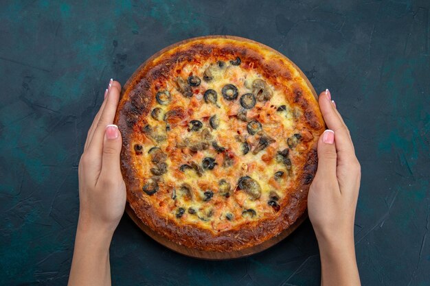 Vista superior de la deliciosa pizza cocida con aceitunas y queso en el escritorio azul oscuro