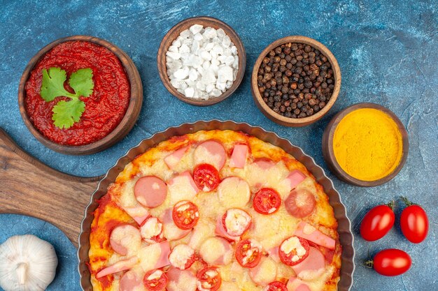 Vista superior de la deliciosa pizza de queso con condimentos y tomates sobre fondo azul, comida italiana, pastel de masa, comida rápida, color fotográfico