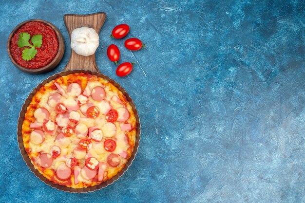 Vista superior deliciosa pizza de queso con salchichas y tomates sobre fondo azul pastel de masa de comida italiana comida rápida lugar libre de color de la foto