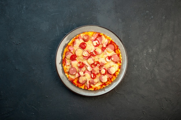 Vista superior de la deliciosa pizza de queso con salchichas y tomates sobre fondo oscuro, comida italiana, pastel de masa, comida rápida, color fotográfico