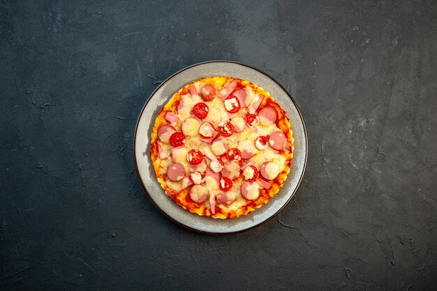 Vista superior de la deliciosa pizza de queso con salchichas y tomates sobre fondo oscuro, comida italiana, pastel de masa, comida rápida, color fotográfico